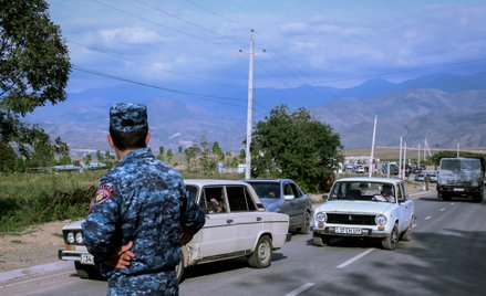 Policjant z Armenii obserwuje pojazdy przewożące uchodźców przybywają do centrum rejestracji w pobli