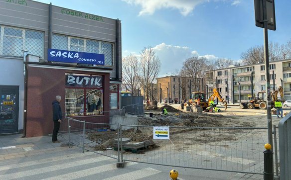 Prowizoryczne znaki informujące o dojściu do sklepów są mocowane trytytkami do metalowych płotów