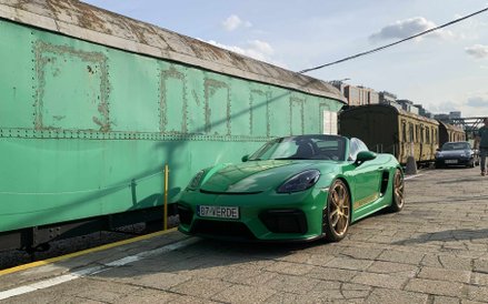 Intensywnie zielone Porsche Cayman ze złotymi felgami, zaparkowane obok zabytkowego, zielonego wagon