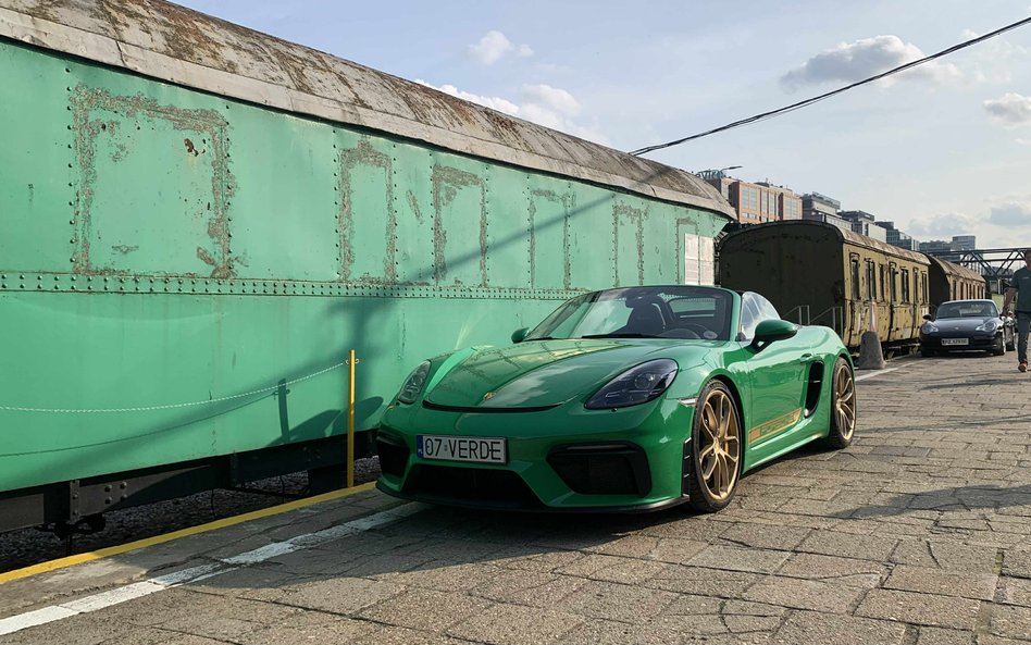 Intensywnie zielone Porsche Cayman ze złotymi felgami, zaparkowane obok zabytkowego, zielonego wagon