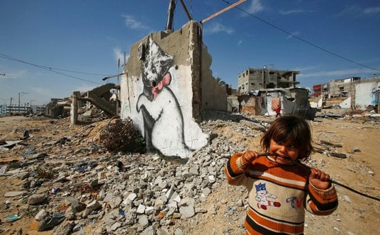 Palestyńska dziewczynka patrzy na mural stworzony przez  Banksy’ego w północnej Strefie Gazy