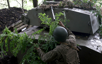 Ukraiński artylerzysta używa gałęzi do kamuflażu pojazdu na linii frontu w pobliżu Bachmutu