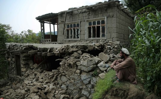 Mężczyzna, siedzący przed zniszczonym domem w prowincji Kunar