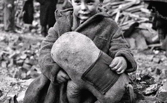 Chłopiec z pluszową zabawką pośród ruin po niemieckim bombardowaniu z powietrza. Londyn, 1940 r.