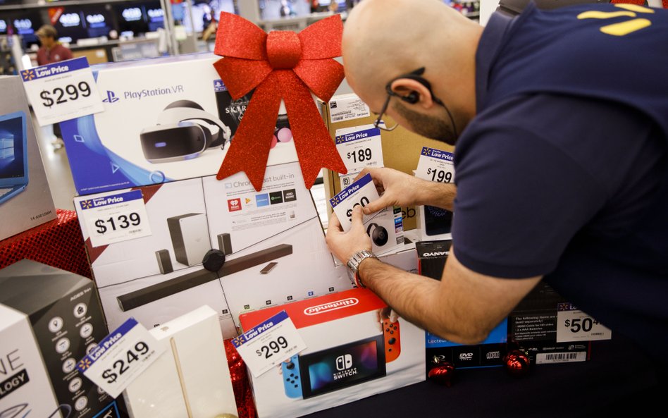 Przygotowania do Black Friday. Pracownik supermarketu z elektroniką przyczepia obniżone ceny do prod