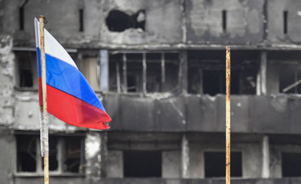 Flaga Rosji na tle zniszczonego budynku w zajętym przez wojska rosyjskie Mariupolu