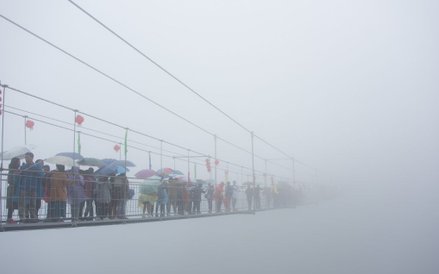 Chińscy turyści przechodzący przez szklany most wiszący nad 180-metrową doliną w górach Shinuizhai w