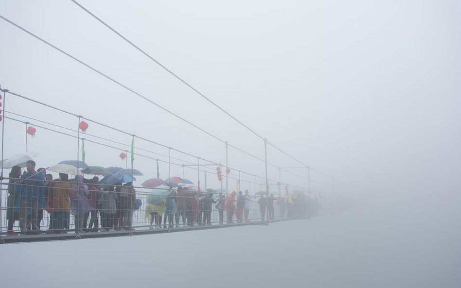Chińscy turyści przechodzący przez szklany most wiszący nad 180-metrową doliną w górach Shinuizhai w