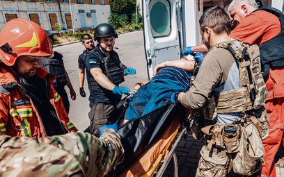 Ratownicy medyczni wnoszą do karetki cywila ranionego przez rosyjską bombę klastrową zrzuconą na Bac