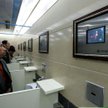 Publiczna toaleta z monitorami telewizyjnymi w ścianie nad każdym pisuarem