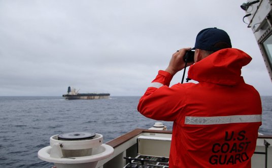 Funkcjonariusz Straży Przybrzeżnej USA patrzy przez lornetkę na statek Marinera (ex-Bella 1)