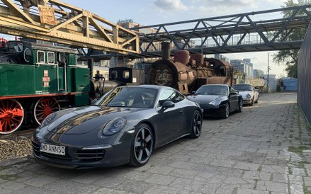 Szereg eleganckich Porsche, w tym ciemnoszare 911 na pierwszym planie, zaparkowanych wzdłuż zabytkow