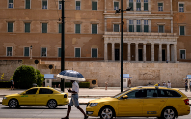Mieszkaniec Aten chroni się przed słońcem podczas fali upałów, która zaatakowała stolicę Grecji na p
