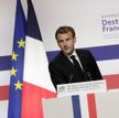 Prezydent Francji Emmanuel Macron przed flagami pokazującymi zarówno stary, jak i nowy odcień niebie