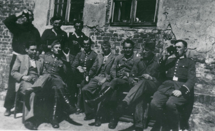 Henryk Mania (pierwszy z lewej) siedzi w jasnym garniturze w otoczeniu esesmanów z załogi ośrodka śm