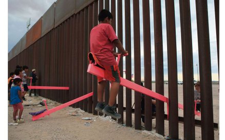 Amerykańskie i meksykańskie dzieci bawią się na huśtawkach zamontowanych na płocie granicznym między