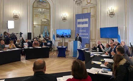 Ilia Ponomariow, główny organizator spotkania, stoi przy mównicy przykrytej flagą „innej Rosji”