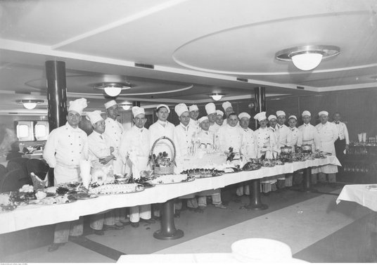 Kuchmistrze w sali restauracyjnej transatlantyku MS Batory. Stół z modelem Batorego wykonanym z masł