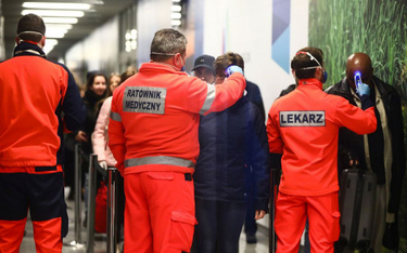 Personel medyczny mierzy temperaturę pasażerom, którzy przylecieli z Mediolanu na lotnisku w podkrak