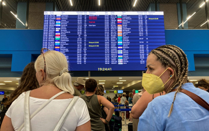 Turyści przed tablicą informacyjną w hali odlotów lotniska podczas ewakuacji z powodu pożarów na gre
