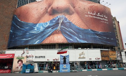 Mężczyzna trzyma flagę Iranu przed bannerem w Teheranie, przedstawiającym prezydenta USA Donalda Tru