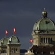 Szwajcarskie flagi narodowe powiewają nad Pałacem Federalnym, budynkiem parlamentu Szwajcarii, w Ber