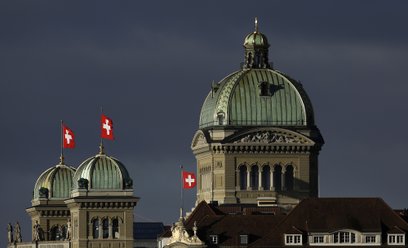Szwajcarskie flagi narodowe powiewają nad Pałacem Federalnym, budynkiem parlamentu Szwajcarii, w Ber