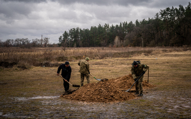 Ukraińscy żołnierze i cywil zakopują trumnę z ciałem ukraińskiego żołnierza, poległego w walkach w o