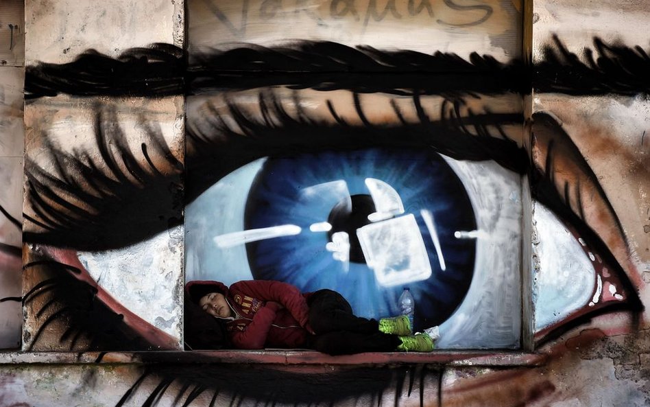Kobieta śpiąca przed graffiti ilustrującym oko, w porcie Mytilene na greckiej wyspie Lesbos.
