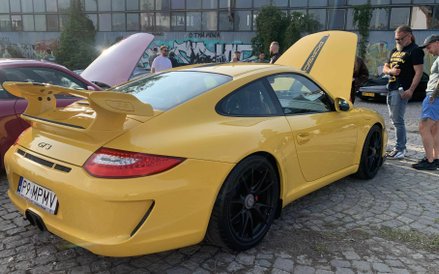 Odważne, żółte Porsche 911 GT3 z podniesioną maską silnika przyciąga wzrok na tle industrialnego oto