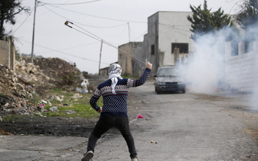 Palestyński protestujący przygotowuje się do rzucenia kamieniem podczas starć z izraelskimi żołnierz