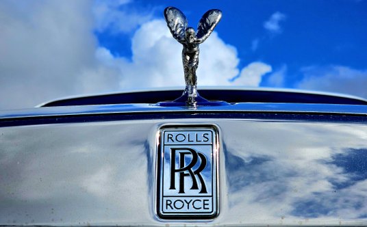 Spirit of Ecstasy ma postać kobiety pochylonej do przodu z ramionami wyciągniętymi do tyłu, falujący