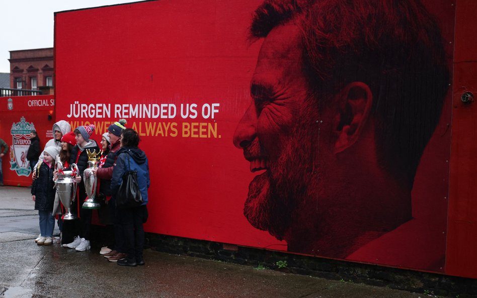 Kibice Liverpoolu pozują do zdjęć z repliką trofeum Premier League i Pucharu Ligi Mistrzów, obok wiz