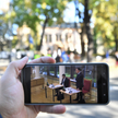 Obrady TK oglądane na ekranie telefonu na tle demonstracji przed siedzibą Trybunału Konstytucyjnego 