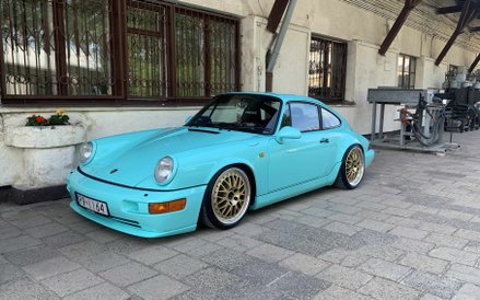 Jasnoniebieskie (aqua blue) Porsche 911 generacji 964, wyposażone w sportowe, złote felgi