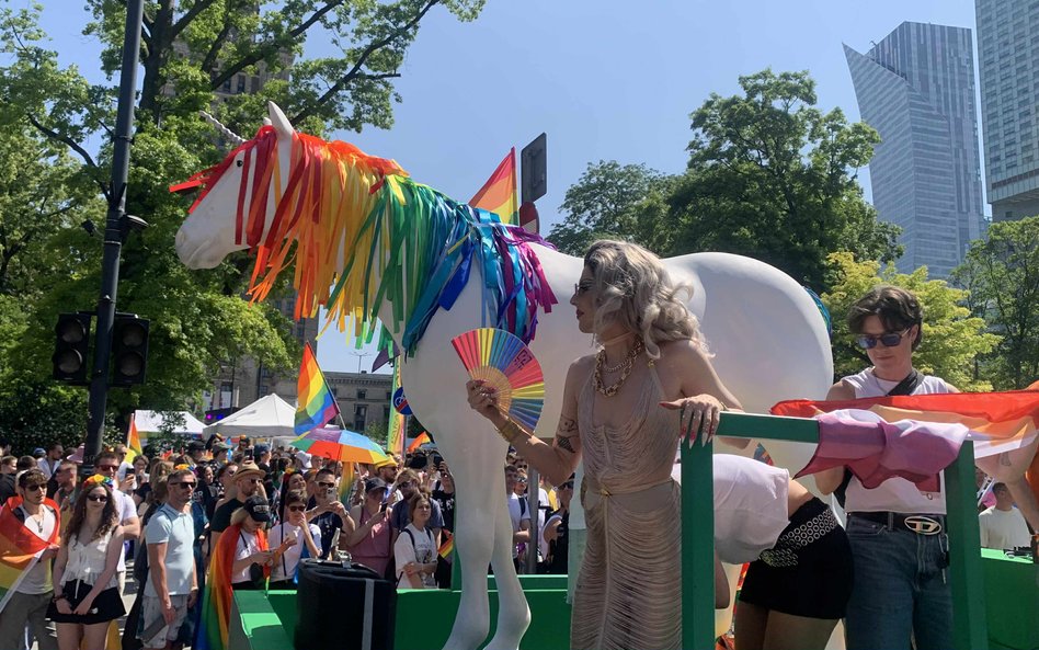 Dekoracja w postaci tęczowego jednorożca i postać w fantazyjnym stroju z tęczowym wachlarzem