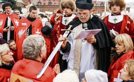 Za ks. Piotrem Natankiem stoją samozwańczy Rycerze Zakonu Chrystusa Króla. Łatwo ich poznać po krwis