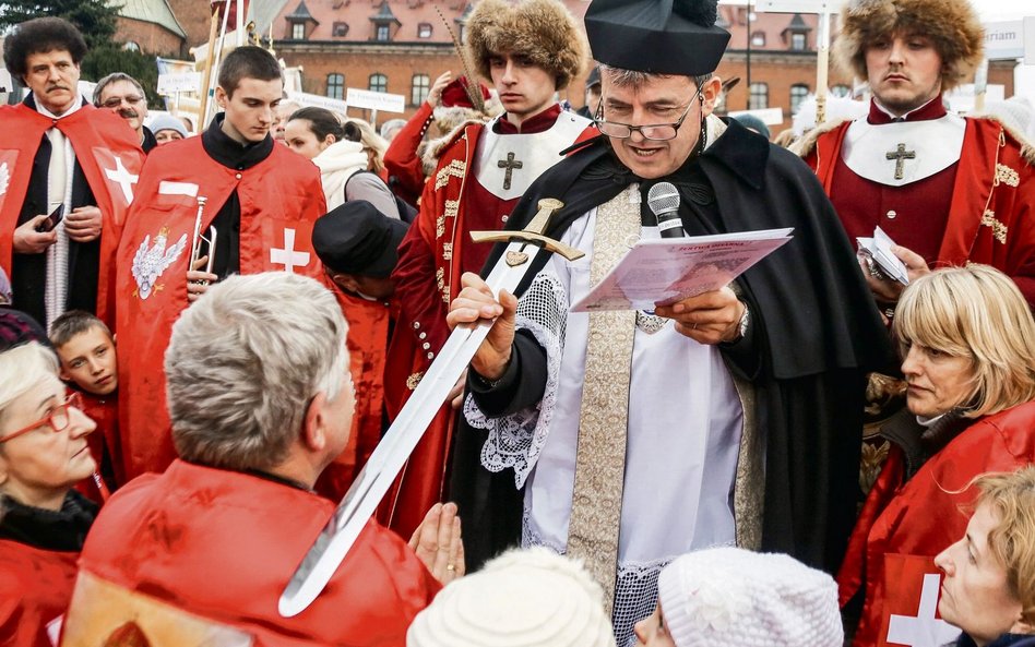 Za ks. Piotrem Natankiem stoją samozwańczy Rycerze Zakonu Chrystusa Króla. Łatwo ich poznać po krwis