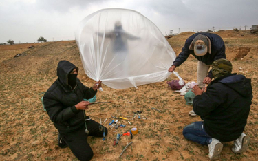 Zamaskowani Palestyńczycy przygotowują łatwopalny obiekt, który wiatr ma zanieść nad tereny Izraela.