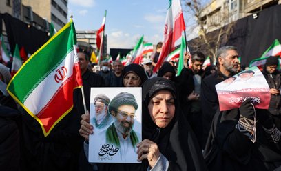 Proreżimowa demonstrantka w Iranie trzyma w ręku grafikę przedstawiającą na pierwszym planie Modżtab