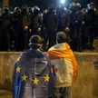 Sandro, owinięty flagą UE, przed szpalerem policjantów na fotografii, która stała się symbolem gruzi