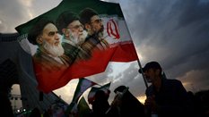 Wiec w Teheranie. Mężczyzna z flagą, na której znajdują się wizerunki ajatollaha Ruhollaha Chomeinie