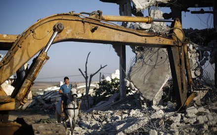 Palestyńczyk jadący konno między gruzami budynków, które zniszczone zostały podczas walk pomiędzy Iz