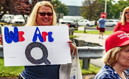 Kobieta trzyma znak „We Are Q” w kolejce do wzięcia udziału w wiecu „Make America Great Again” w Wil