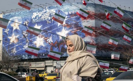 Irańska kobieta przechodzi obok budynku państwowego w centrum Teheranu w Iranie pokrytego gigantyczn