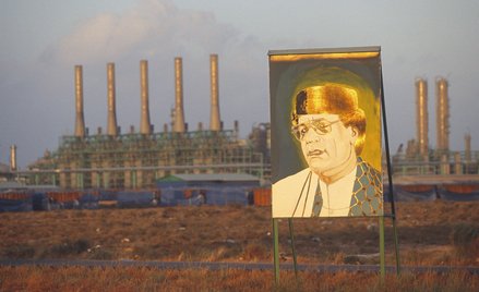 Pozłacany portret libijskiego przywódcy Muammara Kaddafiego (1942–2011) na tle rafinerii ropy naftow