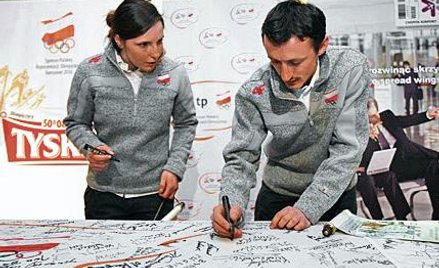 Adam Małysz podpisuje olimpijską flagę. Obok narciarka alpejska Agnieszka Gąsienica-Daniel