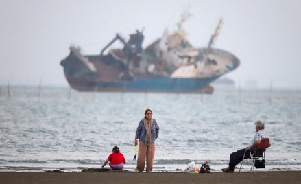 Ludzie gromadzą się na plaży, w pobliżu plaży Bandar Abbas widać statek na Cieśninie Ormuz