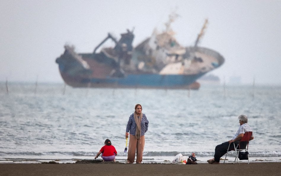 Ludzie gromadzą się na plaży, w pobliżu plaży Bandar Abbas widać statek na Cieśninie Ormuz