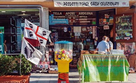 Sardyńskie klimaty. W sklepie wyroby regionalne, przed nim flaga regionu autonomicznego: czerwony kr